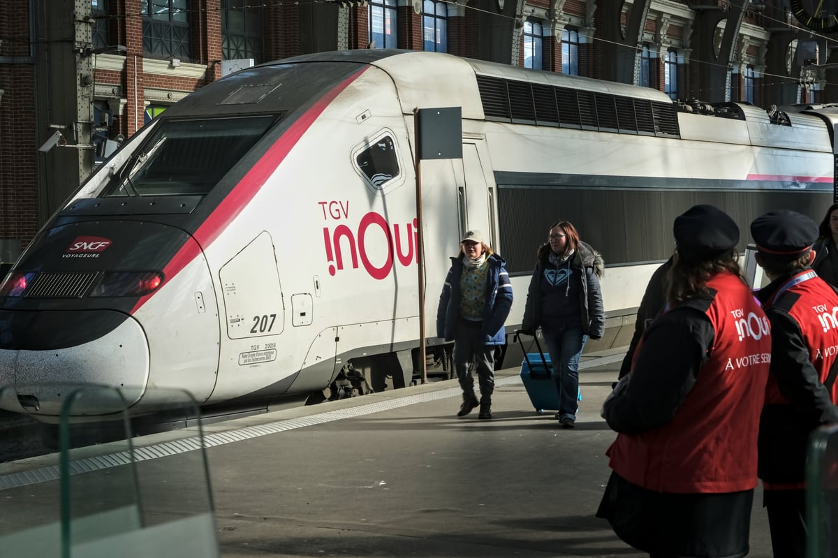 High speed TGV InOui train at a station platform in France with travelers and railway staff during boarding inside a historic terminal
